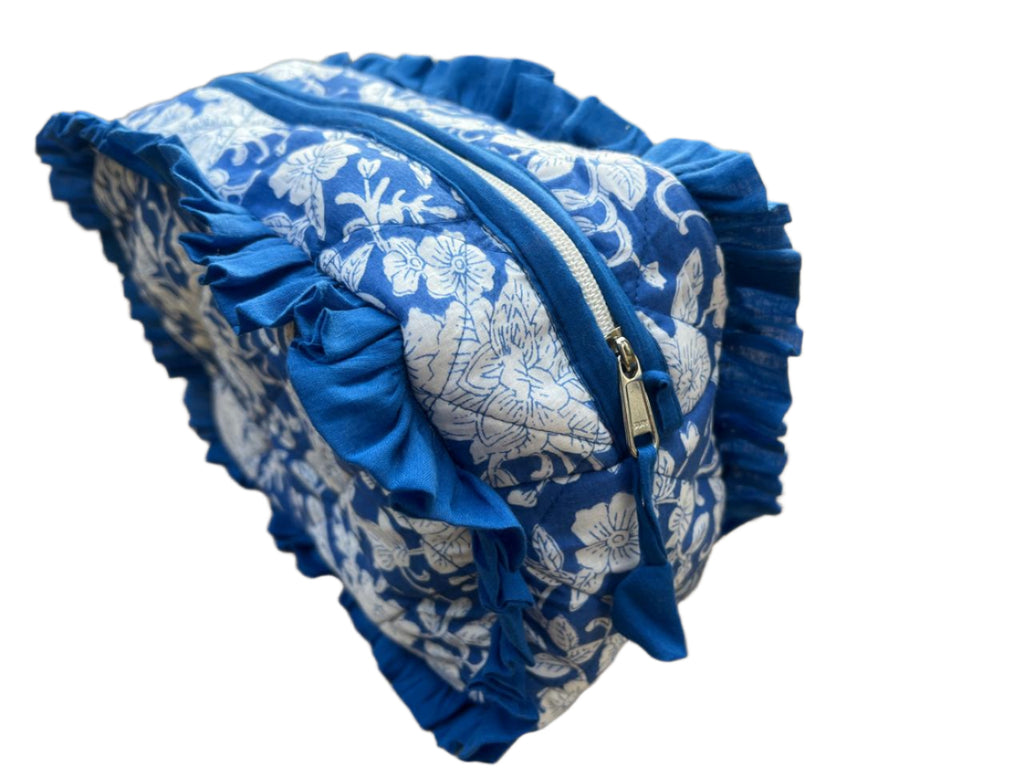 Blue and white floral patterned pouch with ruffles on a sandy ground.