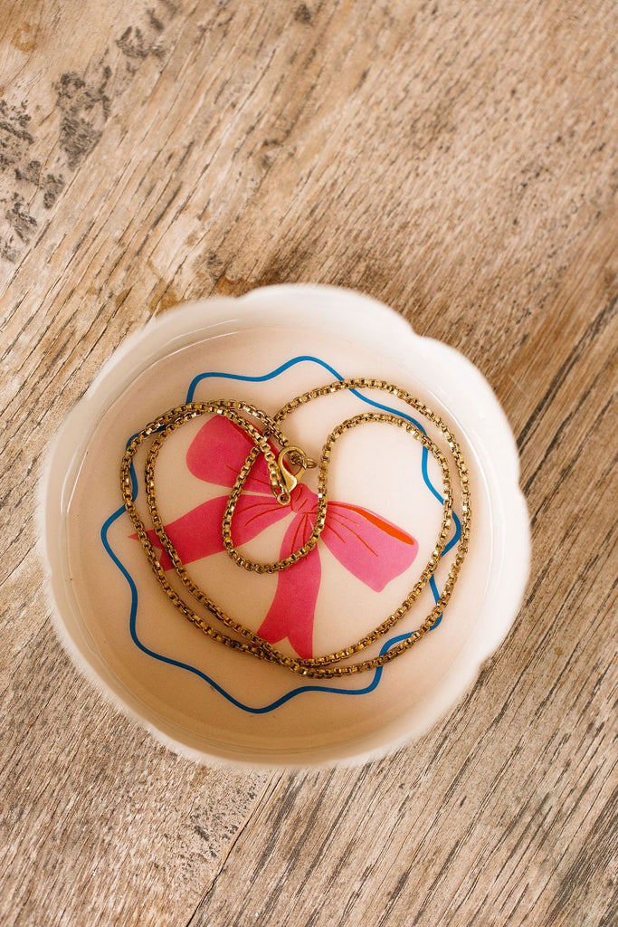 Necklace with a red bow on a decorative plate with heart design on a wooden surface