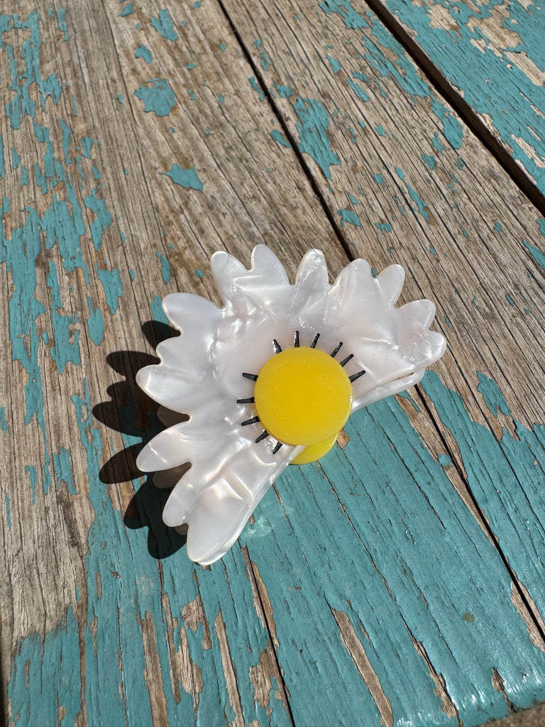 White flower-shaped hair clip on a wooden surface with peeling paint