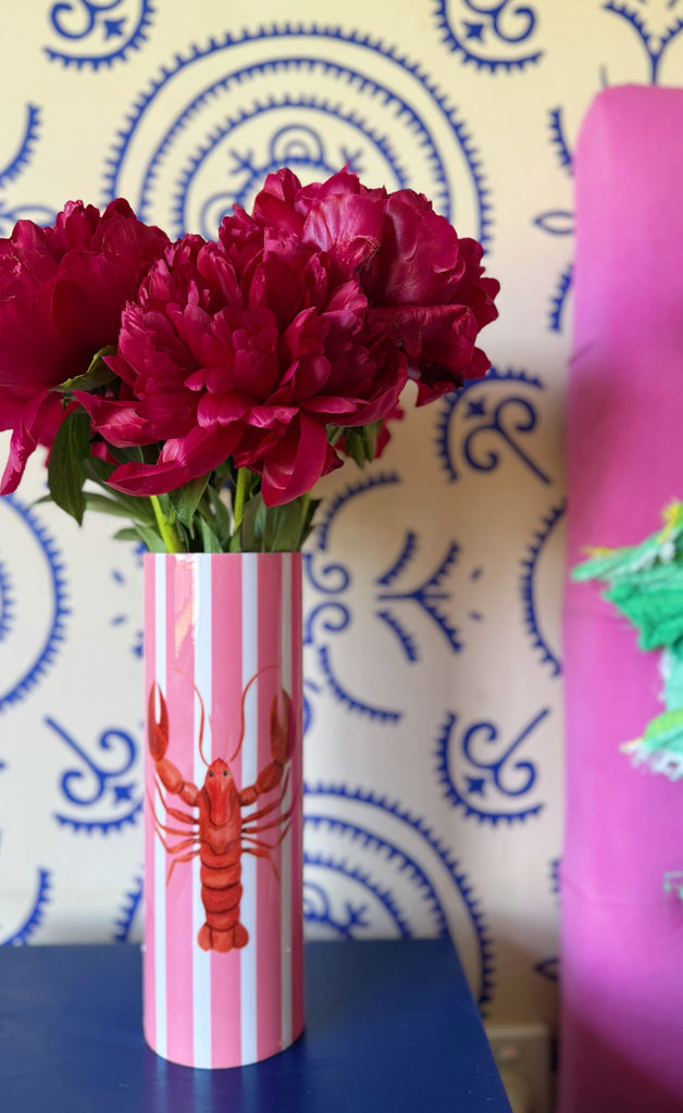 Pink vase with red flowers against a blue patterned wall