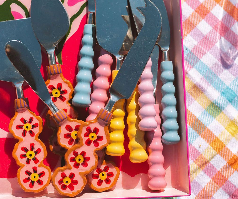 Set of colorful cheese knives with decorative handles in a pink box.